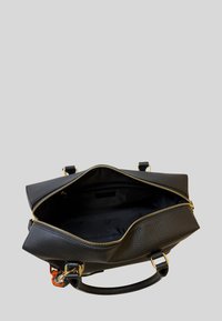 Borsa in pelle nera con cerniera dorata aperta che mostra la fodera interna nera vuota e un piccolo accessorio intrecciato colorato attaccato.