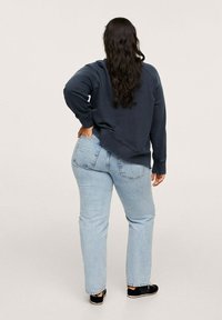 Felpa blu con spalle scese, abbinata a jeans dritti azzurri. Footwear neri completano l'outfit. Sfondo semplice.