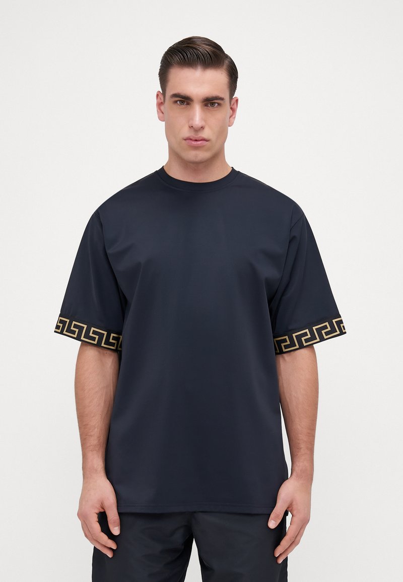 Jūras spēku oversized t-krekls ar īsām piedurknēm, ar zelta ģeometrisku rakstu apkārt piedurkņu malām. Gluda auduma tekstūra, ar apaļu kakla izgriezumu.