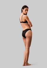 Ensemble de lingerie noire comprenant un soutien-gorge simple avec des bretelles réglables et des culottes bordées de dentelle, mettant en avant une texture lisse et un design minimaliste.