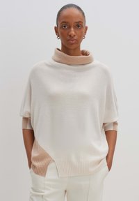 Übergroßer cremefarbener Pullover mit Schalkragen, der einen hellbeigen Akzent am Saum und an den Ärmeln hat. Weicher Stoff und lässige Passform.