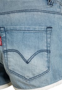 Lichtblauwe denim shorts met een achterzak met een V-vormig stikselpatroon en een klein rood merketiket. De stof lijkt iets vervaagd.