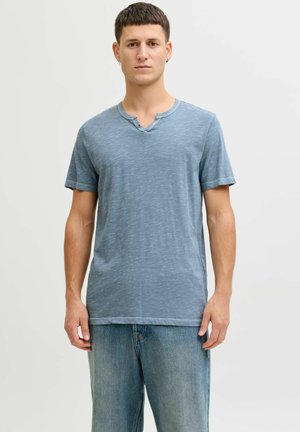 Camiseta azul de manga corta con una sutil textura jaspeada, que presenta un cuello redondo con un detalle de dos botones, combinada con jeans azul claro.