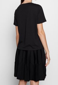 Svart t-shirt med kort ärm och rund halsringning, kombinerad med en knälång svart plisserad kjol som har texturerade vertikala detaljer.