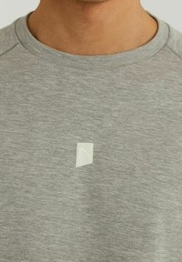 Graues, kurzärmliges T-Shirt aus weichem Stoff, mit einem kleinen weißen geometrischen Logo auf der Brust.