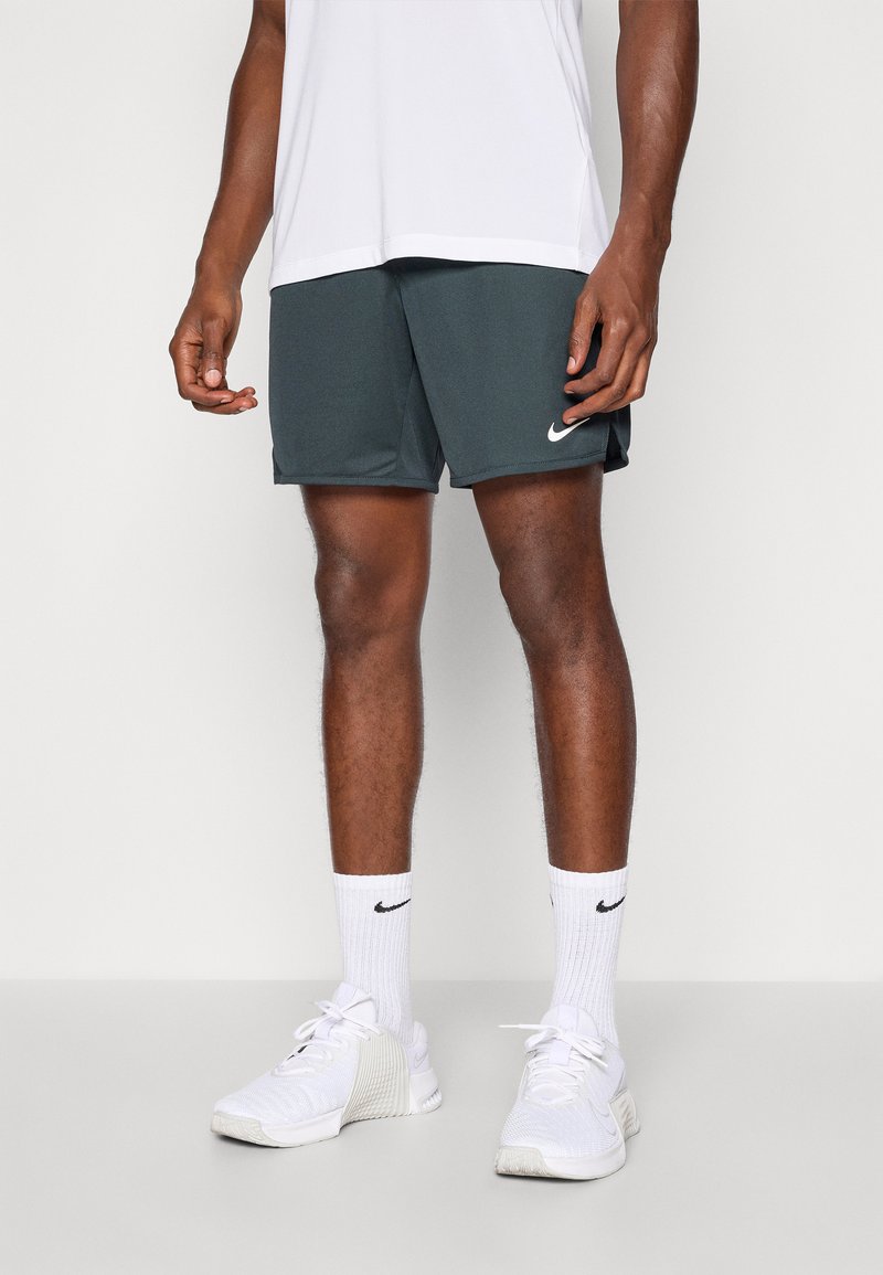 Donkergroene sportshorts met een elastische tailleband en zijzakken, gecombineerd met witte Nike-sokken en witte sneakers.