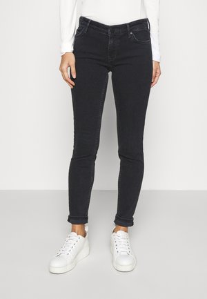 Jeans ajustados negros de cintura alta con tejido elástico, cinco bolsillos y dobladillos enrollados, combinados con zapatillas blancas de caña baja.