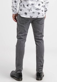 Vaqueros gris slim fit con una textura suave, diseño de cinco bolsillos y detalles de costura sutiles, combinados con zapatos de vestir negros.
