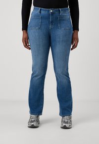 Vaaleansinisiä farkkuja, joissa on suora lahje, ja jotka sisältävät kaksi etutaskua sekä napin sulkemisen. Yhdistetty harmaisiin urheilukenkiin.