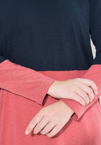 Halenka s dlouhým rukávem, která má tmavě modrou horní část a korálově růžovou spodní část. Měkká, strukturovaná tkanina s designem v barevných blocích.