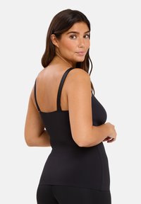 Haut sans manches noir au design ajusté, fabriqué en tissu lisse. Présente des fines bretelles et un ourlet droit à la taille.