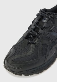 Black athletic shoe featuring a mesh upper, textured accents, and reinforced toe area. Laces and a logo are visible on the side.