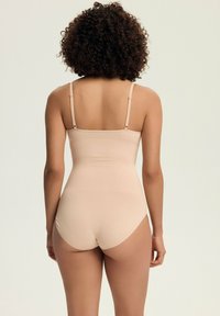 Beige bodysuit with thin adjustable straps and smooth fabric, featuring a fitted design that hugs the body, showcasing a seamless finish.