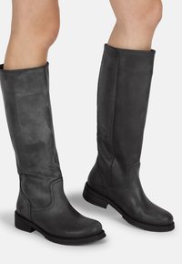 Botas de cuero negro hasta la rodilla con una textura suave, costuras curvas, punta redondeada y un tacón de bloque bajo. Diseño clásico sin herrajes visibles.