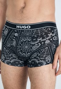 Crne bokserice s uzorkom bandane s bijelim paisley i dizajnom paučine. Elastičan pojas s oznakom "HUGO."