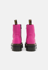 Stivaletti alla caviglia in pelle rosa con una suola nera ampia, dotati di una chiusura con cerniera e un pratico tassello giallo. Cuciture visibili in colori a contrasto.