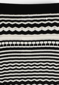 Tissu tricoté en noir et blanc avec des rayures horizontales, des motifs en zigzag et de petites formes géométriques, présentant un seul bouton blanc près du haut.