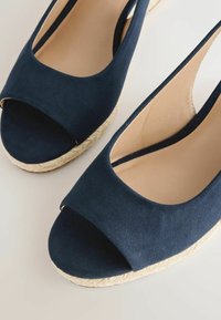 Marineblauwe open-toe slingback espadrille wedges met beige binnenzolen en gevlochten jute plateauzolen op een lichte achtergrond.