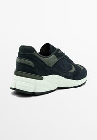 Sneaker in suede blu scuro con accenti verdi, suola in gomma, tomaia texture e design della punta arrotondata. Presenta cuciture dettagliate e un tallone imbottito.