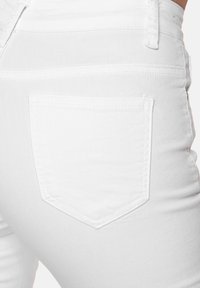 Jeans de mezclilla blanca con un bolsillo trasero de forma rectangular, costuras visibles y textura suave.