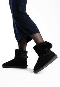 Bottes de cheville en suédine noir avec un accent en fourrure au niveau du haut, des détails texturés sur le côté et une semelle en caoutchouc plate.