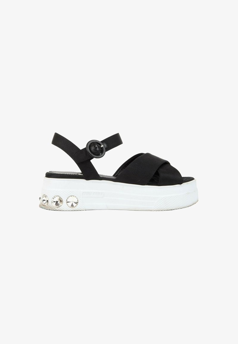 Sandale plateforme noire avec brides croisées, boucle à la cheville, semelle blanche et grandes décorations rondes en cristal sur le talon.