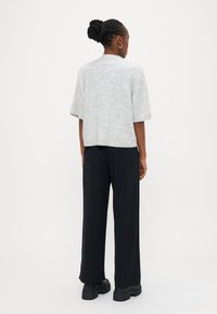 Ανοιχτό γκρι τοπ με κοντά μανίκια σε άνετη γραμμή, συνδυασμένο με μαύρο παντελόνι φαρδιάς γραμμής και χοντρά μαύρα παπούτσια, εμφανιζόμενο από πίσω.