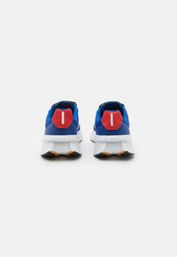 Sapatos desportivos azuis com um acento vermelho no calcanhar, entressola branca e sola de borracha preta. Apresentam um calcanhar plano proeminente e materiais texturizados.