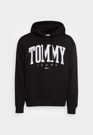 Zwarte hoodie met voorzak, witte "TOMMY JEANS" letters en een klein rood-wit-blauw vlaglogo onder de tekst.