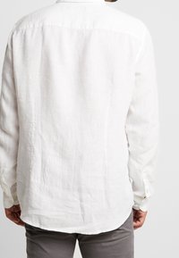 Witte linnen blouse met lange mouwen, knoopmanchetten, een gebogen zoom en een eenvoudige kraag. Getextureerde stof met een lichte, luchtige uitstraling.