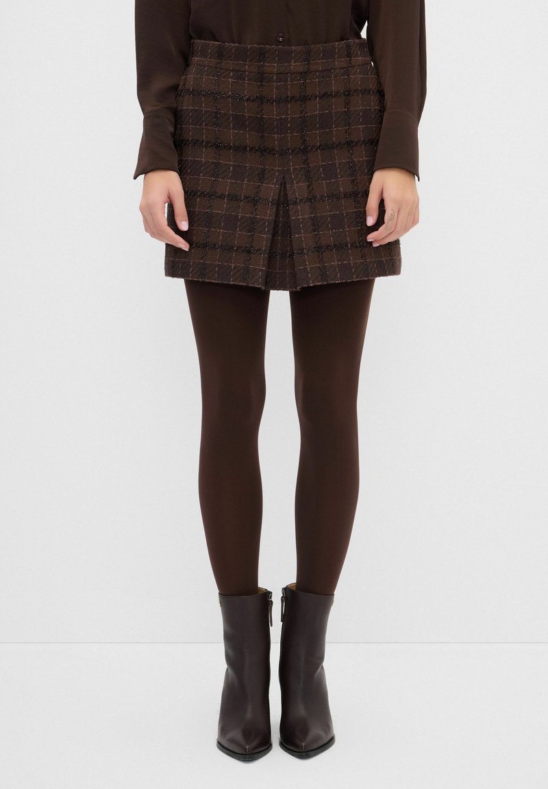 Minifalda de cuadros marrón hecha de tejido texturizado, con un pliegue frontal. Combinada con medias oscuras marrones y botines con cremallera.