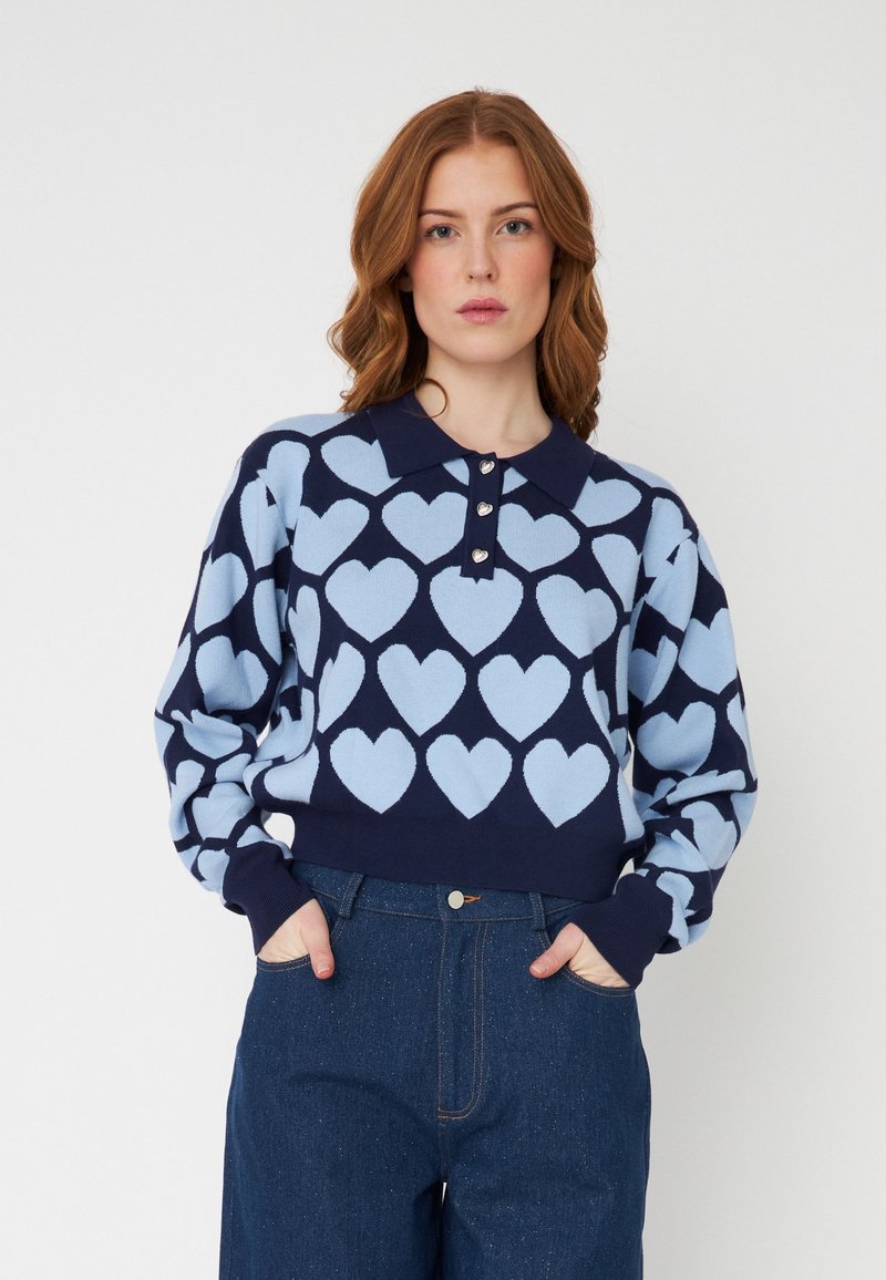 Sweater com uma base azul-escura, apresentando padrões de corações azul-claro, gola com colarinho e três botões metálicos. Textura de malha macia.