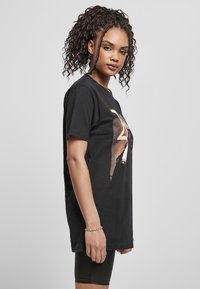 T-shirt oversized en coton noir avec un imprimé graphique à l'avant, des manches courtes et un col rond. Design simple et décontracté.