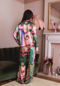 Buntes Satin-Pyjama-Set mit auffälligen geometrischen Mustern, Sternen und Sonnenmotiven in Pink, Grün und Blau. Locker sitzendes Langarmoberteil.