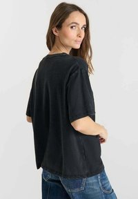 Camiseta negra de gran tamaño con cuello redondo y mangas cortas, que cuenta con una tela suave y texturizada. La parte posterior tiene un ligero dobladillo en caída.