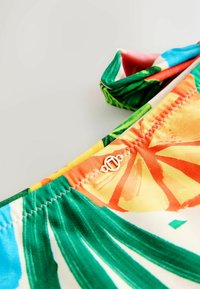 Kolorowy top bikini z tropikalnymi wzorami owoców i liści. Wykonany z miękkiej tkaniny z detalem w postaci złotego elementu w centrum.