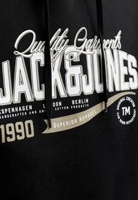 Sweat à capuche noir avec texte blanc et beige indiquant "Quality Garments JACK & JONES" et noms de villes Copenhague, Londres, Berlin, avec cordons.