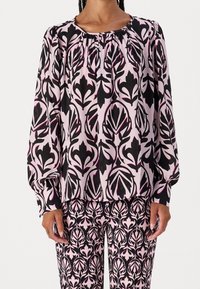 Blouse à manches longues et pantalon assorti dans un motif floral rose et noir. Le tissu est doux, avec des détails froncés au niveau du cou.