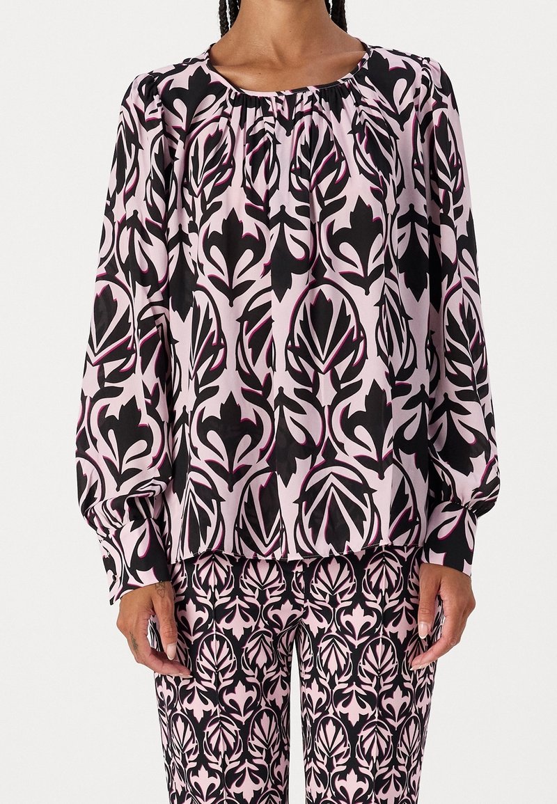 Blouse à manches longues et pantalon assorti dans un motif floral rose et noir. Le tissu est doux, avec des détails froncés au niveau du cou.