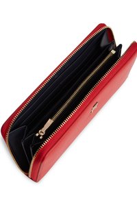 Πορτοφόλι από κόκκινο δέρμα με φερμουάρ που περιβάλλει, εσωτερικό σε μαύρο χρώμα, πολλαπλές θήκες για κάρτες και φερμουάρ σε χρυσό τόνο με λογότυπο.