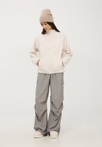 Giacca a zip in pile rosa chiaro con tasche laterali, abbinata a pantaloni cargo grigi larghi e un berretto beige, caratterizzata da una vestibilità comoda.