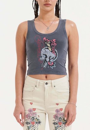 Top court gris avec un design graphique représentant un crâne orné d'un papillon et d'accents floraux. Porté avec un jean taille haute de couleur claire.