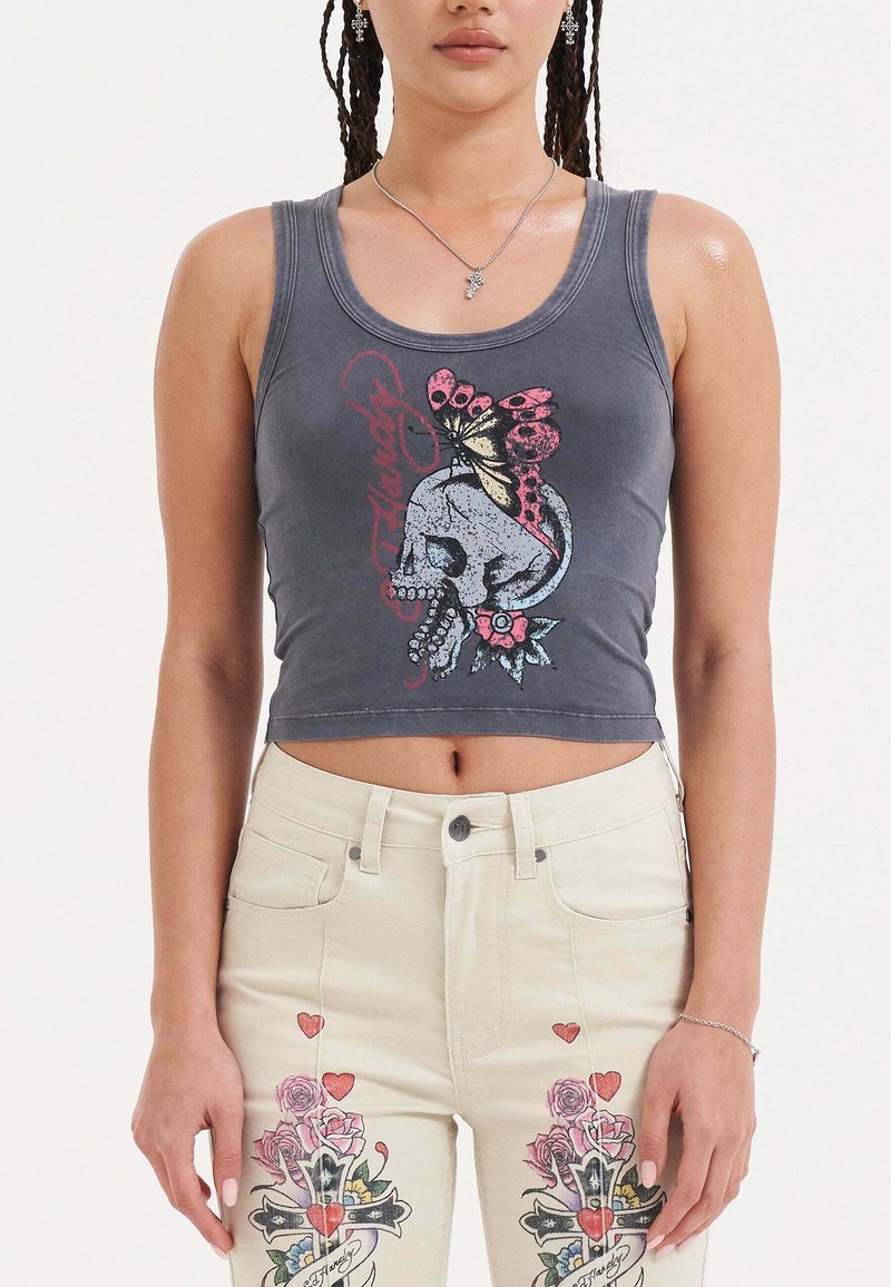 Top court gris avec un design graphique représentant un crâne orné d'un papillon et d'accents floraux. Porté avec un jean taille haute de couleur claire.