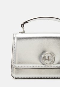 Sac à main métallique argenté avec un design structuré, doté d'une poignée supérieure, de bords cousus et d'un accent de logo circulaire à l'avant.