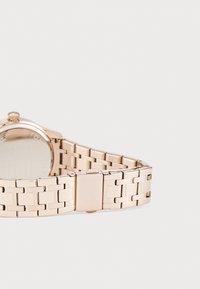 Reloj de pulsera en oro rosado con una pulsera de eslabones metálicos de acabado cepillado, una caja redonda y un detalle de cierre pulido. Pantalla de cristal clara visible.
