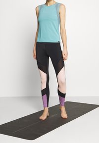 Světle modrý top bez rukávů s síťovanými detaily, spárovaný s černými legínami se geometrickými barevnými bloky v jemně růžové a fialové.