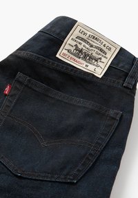 Jeans in denim blu scuro con taglio dritto. Presentano una tasca posteriore cucita e un'etichetta rettangolare con il marchio e le istruzioni per la cura.