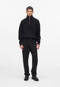 Pulover negru din tricot cu guler înalt și fermoar argintiu, asortat cu pantaloni negri texturați, având un model subtil cu dungi fine și accente metalice.