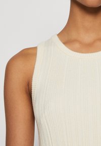 Ριγέ αμάνικο μπλουζάκι σε εκρού, με στρογγυλή λαιμόκοψη. Το ύφασμα φαίνεται μαλακό με υφή.