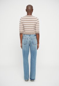 Beige gestrickter, kürzerer Pullover mit weißen horizontalen Streifen, kombiniert mit hellblauen, hochgeschnittenen Jeans mit geradem Bein.